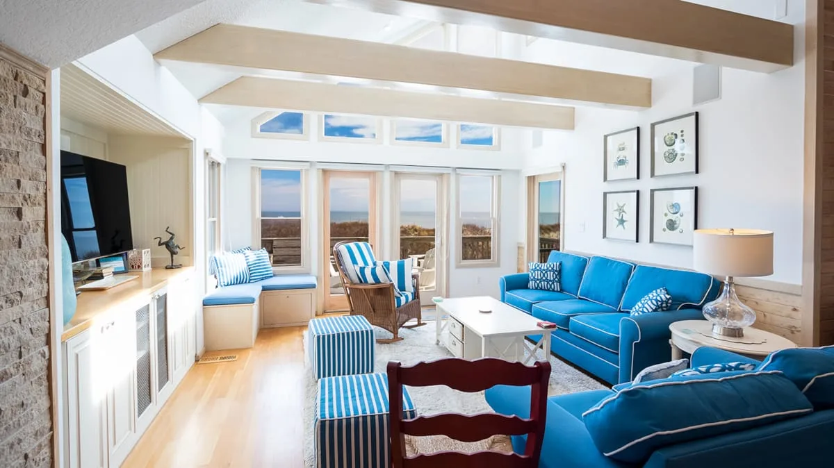 Una sala de estar luminosa con asientos azules y ventanas con vistas al agua.