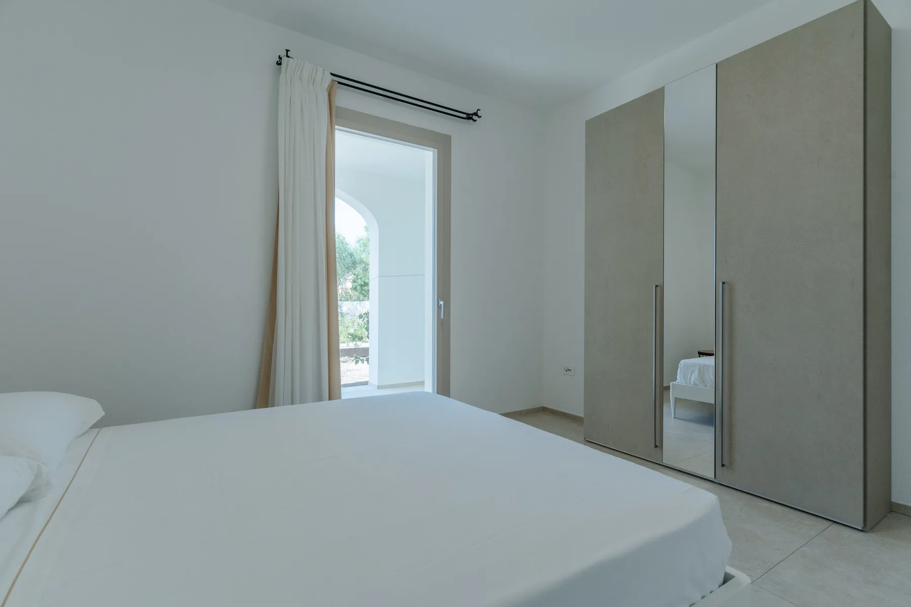 Un dormitorio luminoso con una cama, armarios altos y una ventana.