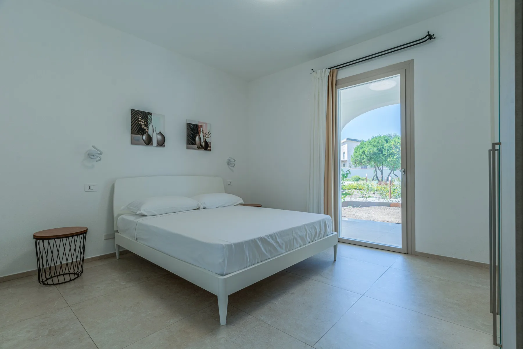 Un dormitorio luminoso con una cama junto a una puerta de vidrio que da a un patio.