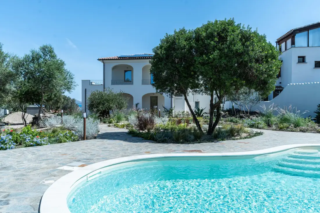 Una piscina al aire libre junto a un patio pavimentado y un jardín ajardinado.