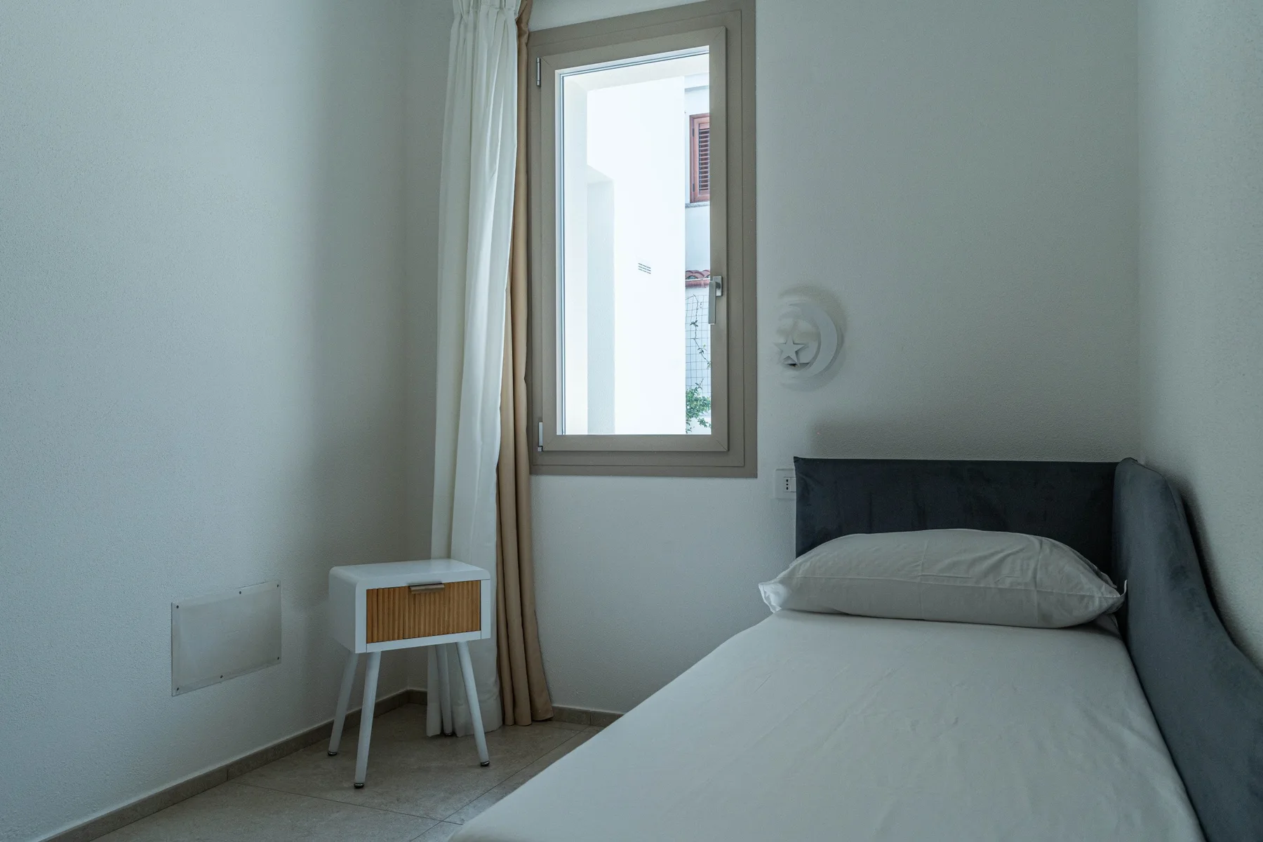 Un dormitorio con una cama junto a una ventana y una pequeña mesita de noche.