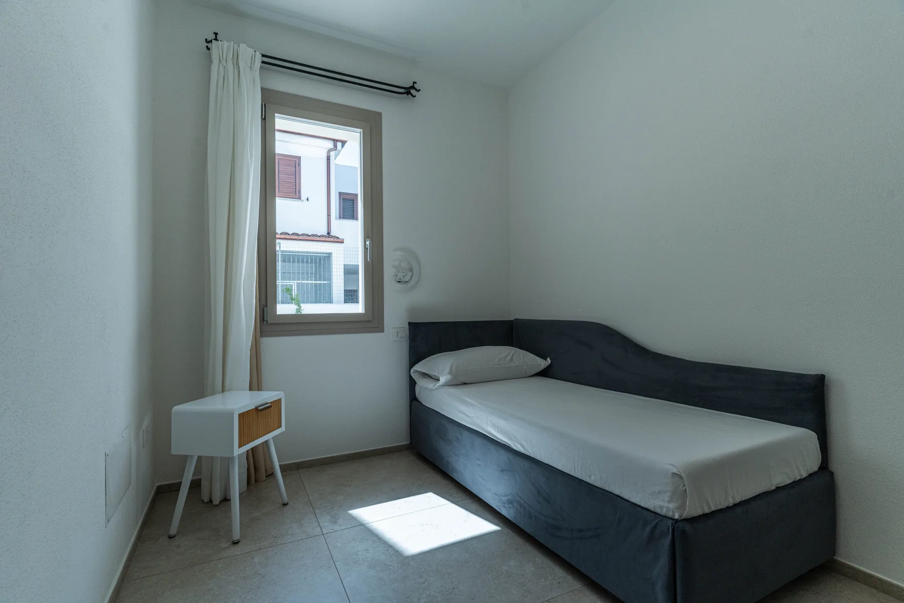 Un dormitorio pequeño con una cama individual junto a una ventana y una mesa pequeña.