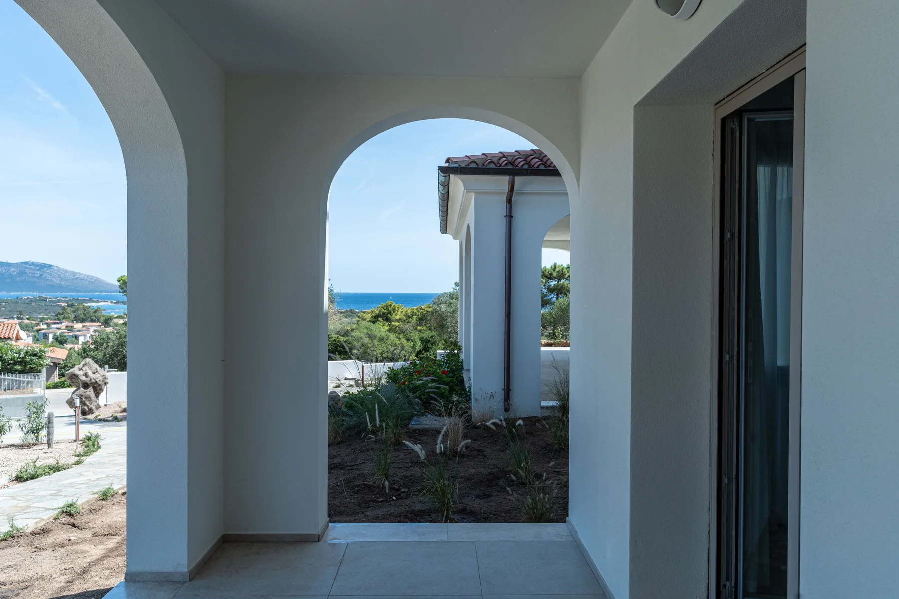 Un patio cubierto con arcos da a un jardín y al mar.