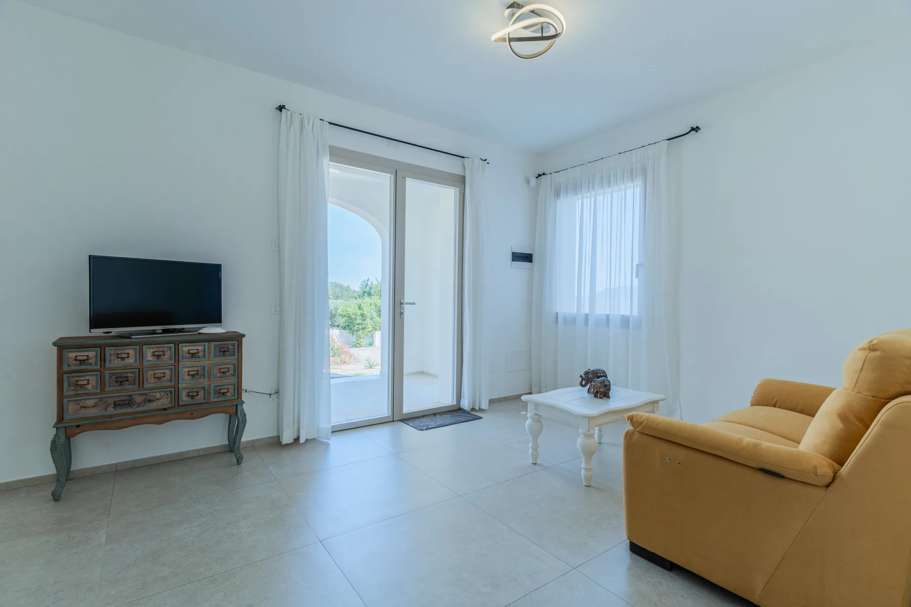 Una sala luminosa con asientos, un televisor y puertas de vidrio que dan a un balcón.