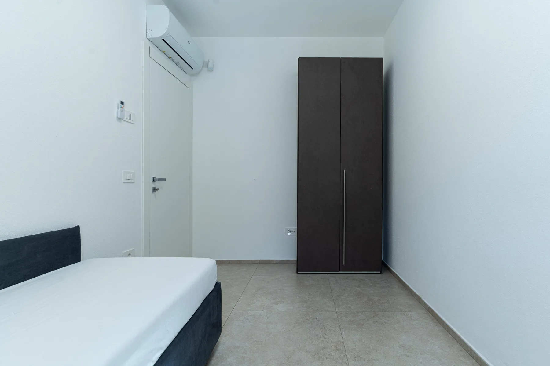 Un dormitorio sencillo con una cama y un armario alto y oscuro.