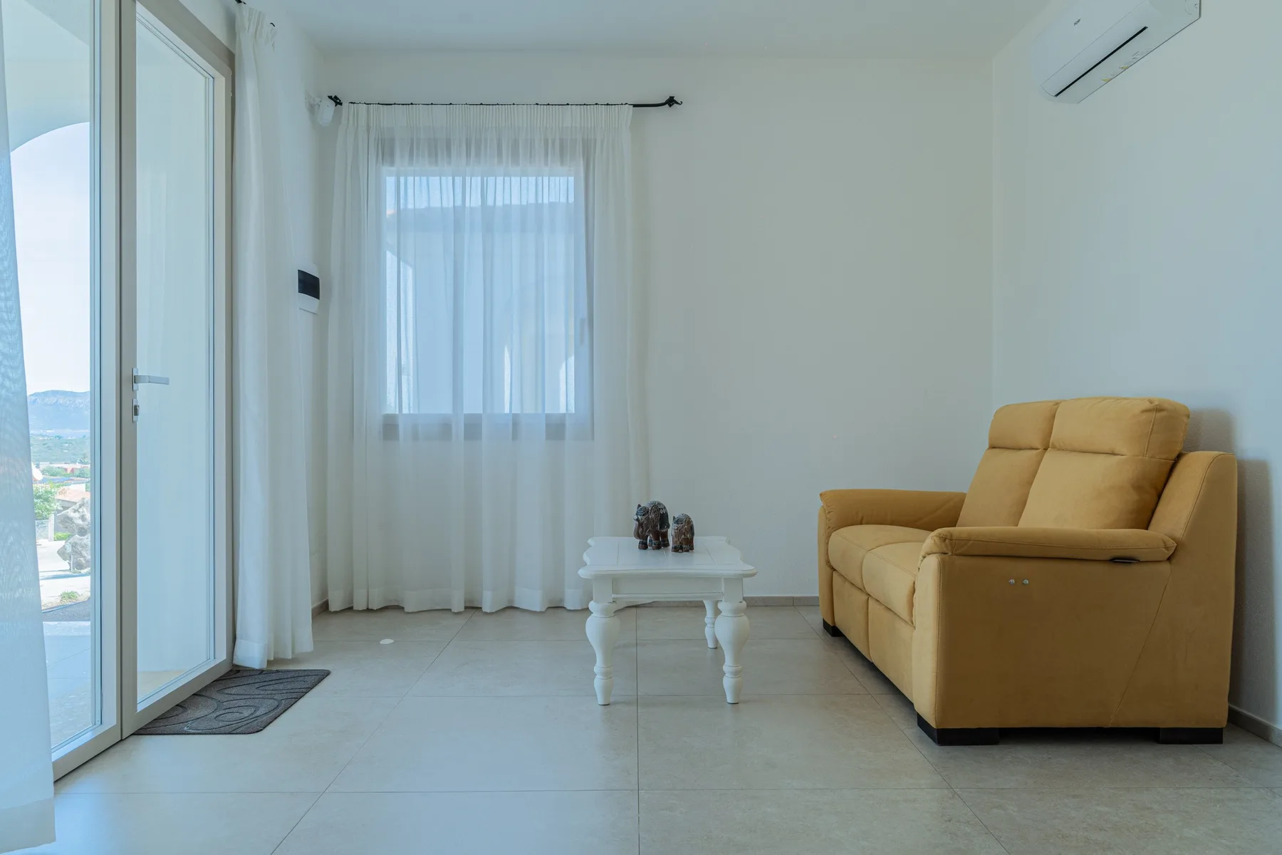 Una sala luminosa con un sofá amarillo y una pequeña mesa blanca.