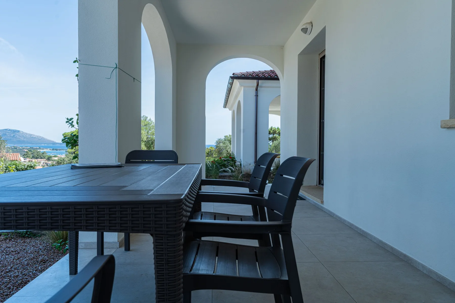 Comedor exterior cubierto con una mesa y asientos oscuros junto a aberturas en arco.