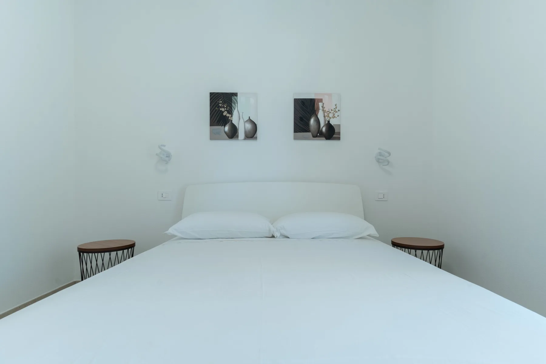 Un dormitorio con una cama bien tendida y dos cuadros enmarcados sobre el cabecero.