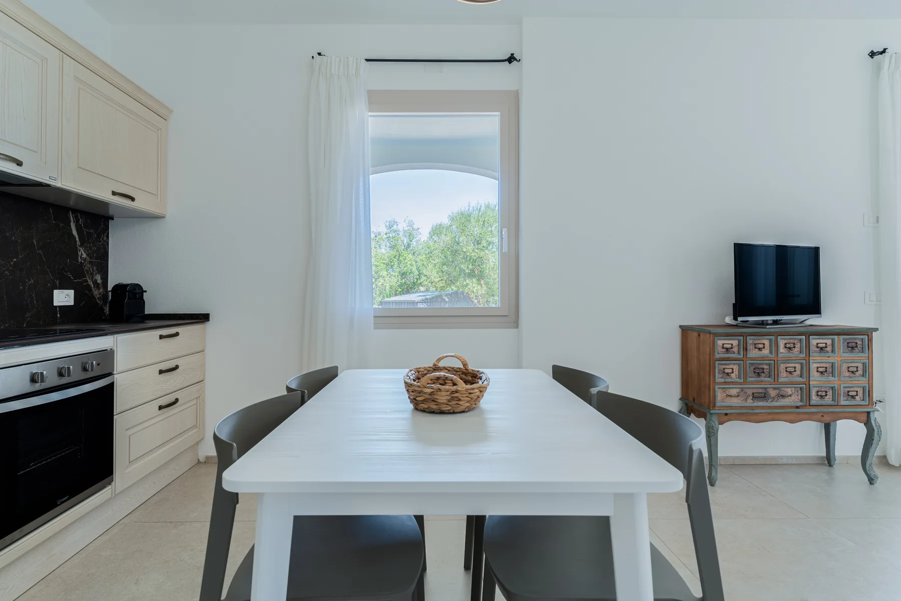 Comedor con una mesa blanca y una ventana con vistas a la vegetación.