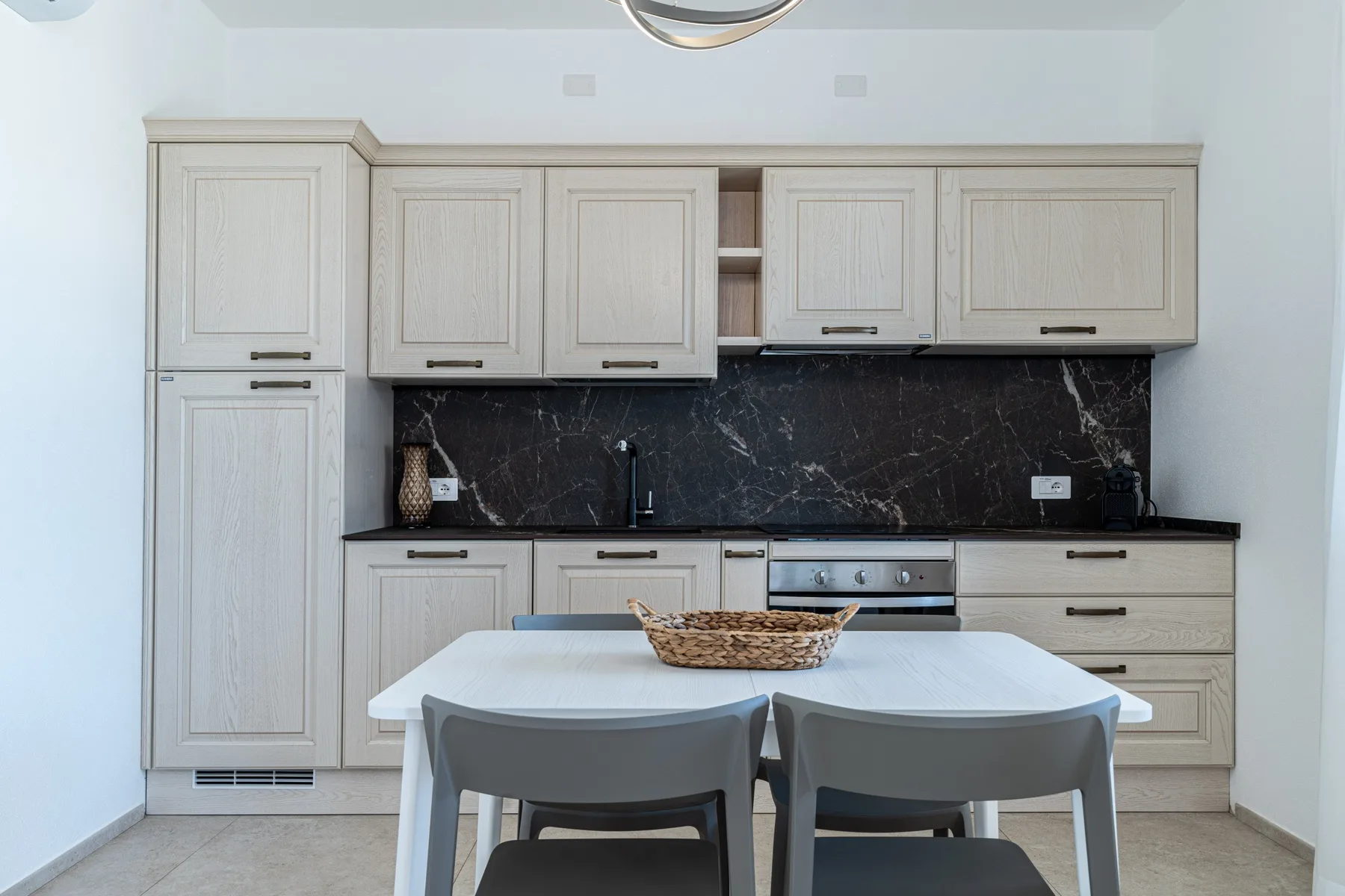 Una cocina luminosa con gabinetes claros, encimeras oscuras y una mesa de comedor.