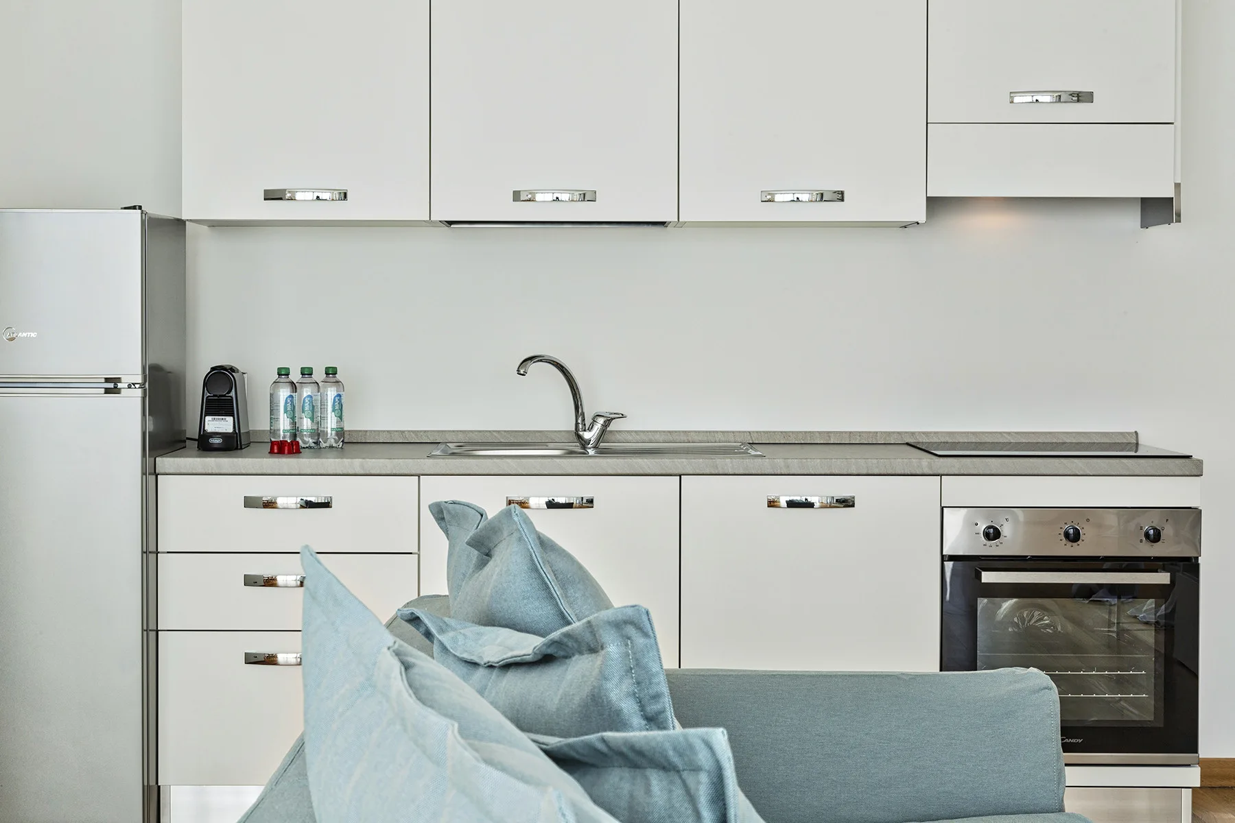 A modern kitchen with white cabinetry and a sink, viewed behind blue seating.