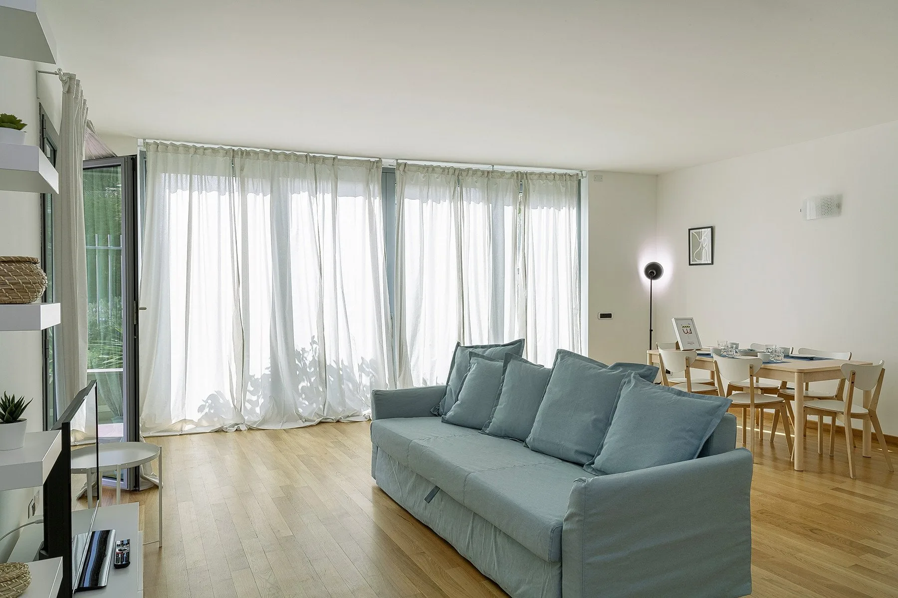 Una luminosa sala de estar y comedor con un sofá junto a una mesa de madera.
