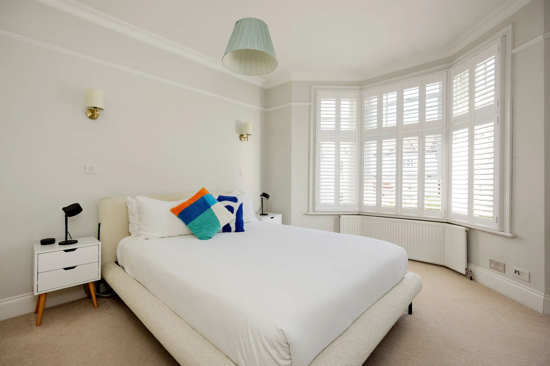 A bright bedroom with a neatly made bed and large shuttered windows.