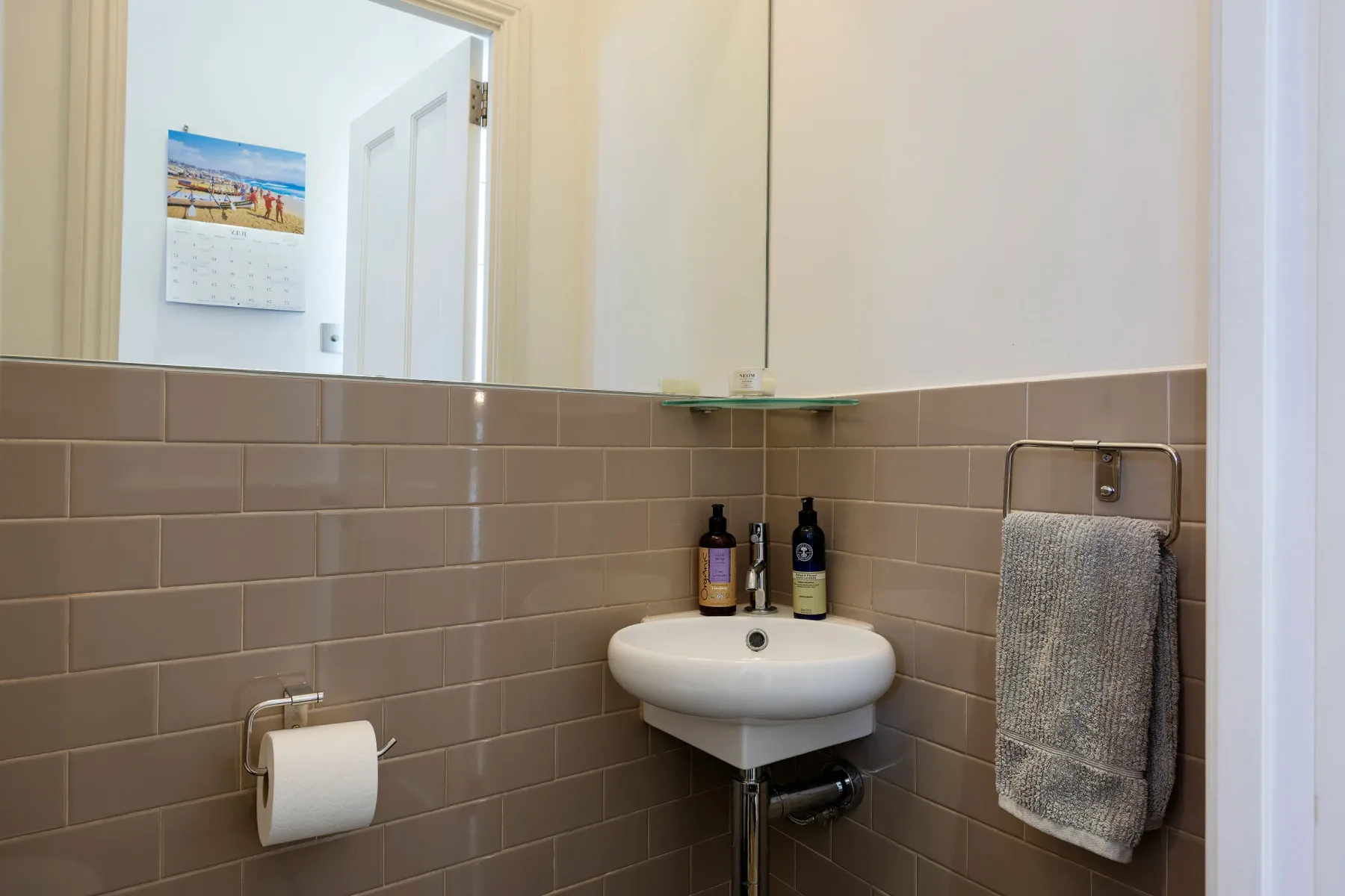 A bathroom sink sits above tiled walls beside a towel rack.