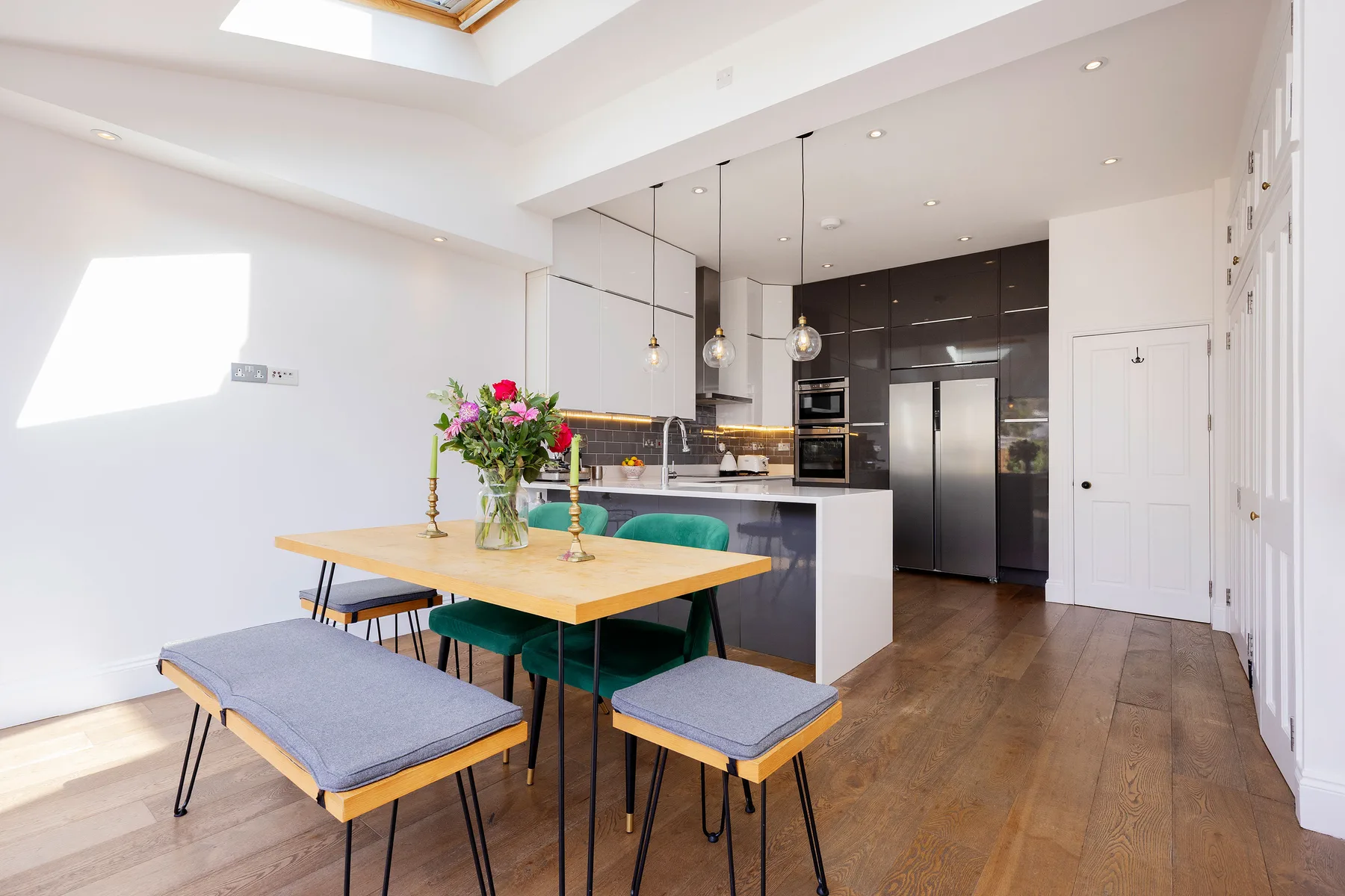 A bright dining area with a wooden table and an open kitchen behind it.