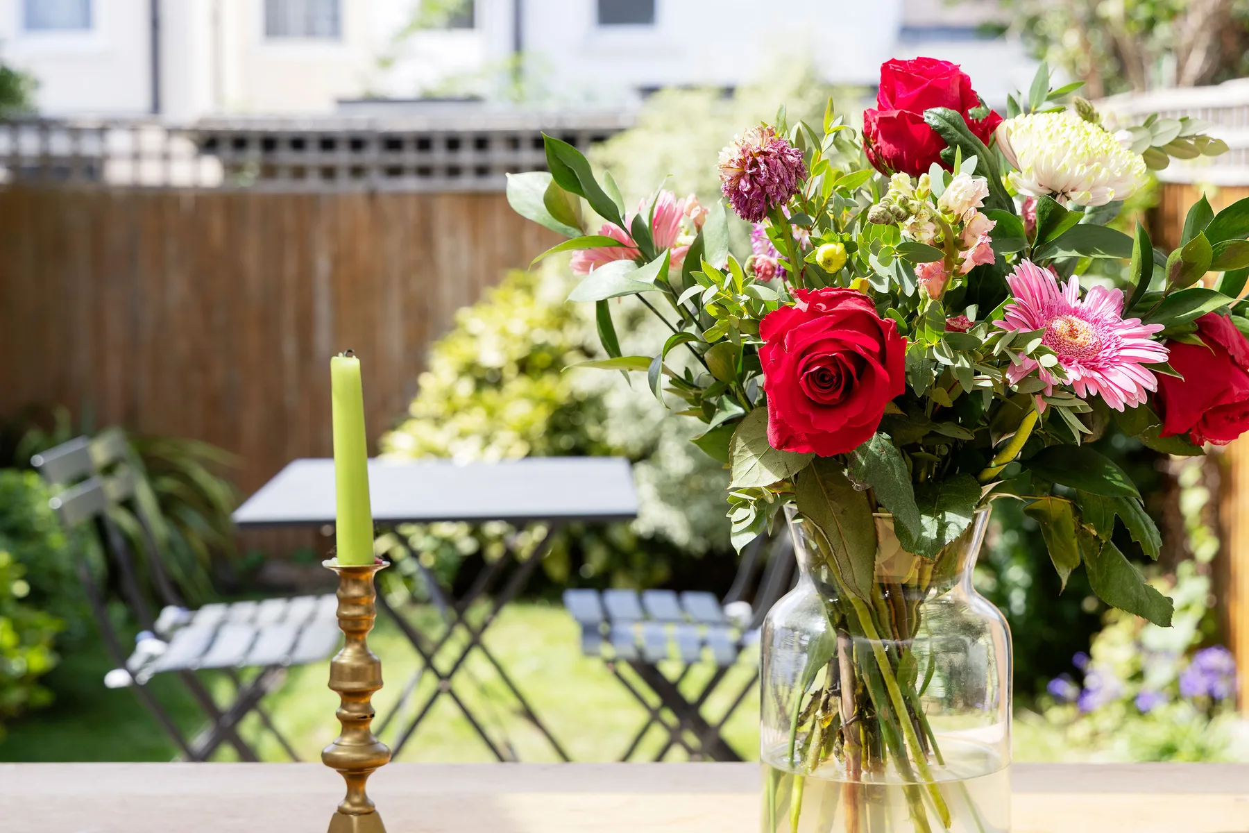 A flower arrangement in a glass vase sits on a table in a garden.