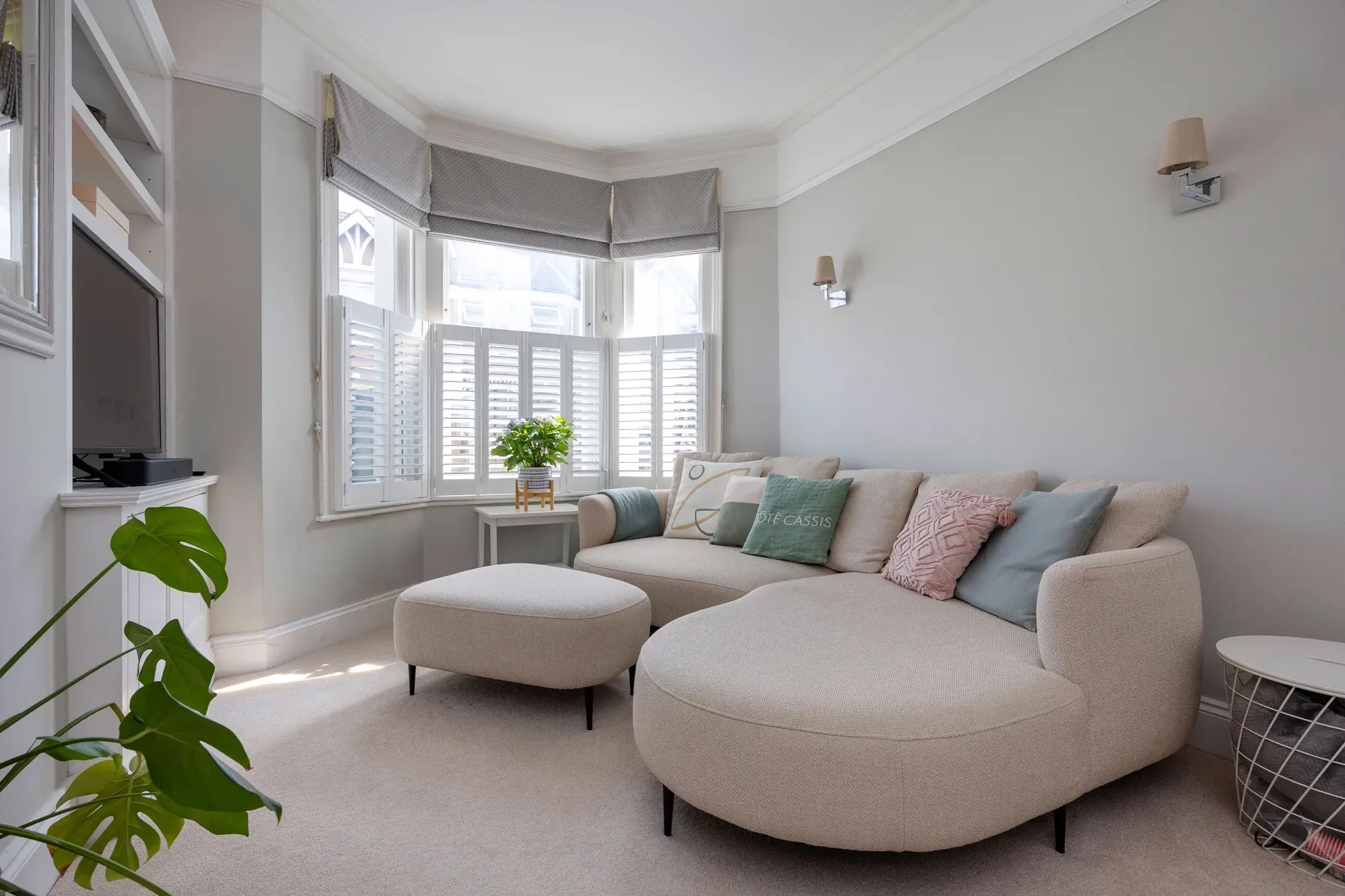 A bright living room with a curved sectional and large shuttered windows.