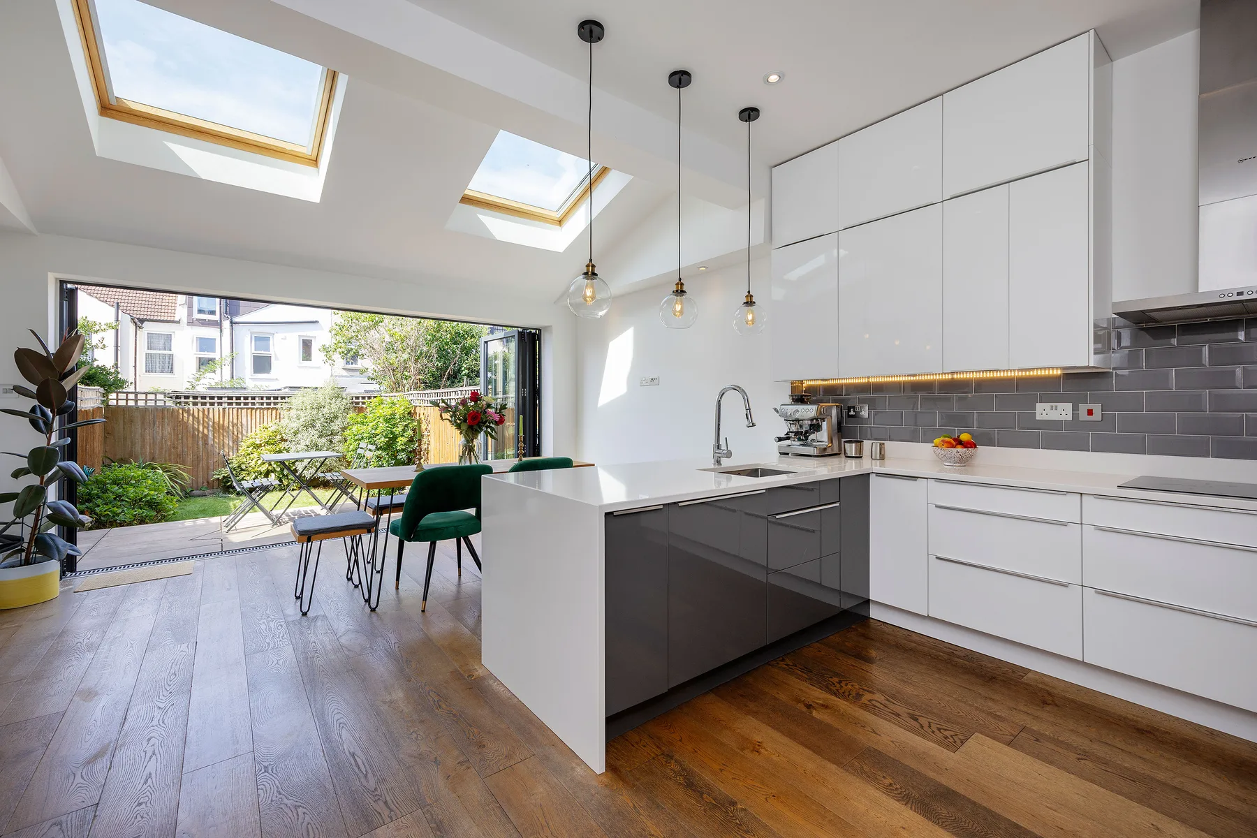 A bright modern kitchen opens onto a dining area and a garden-facing patio.