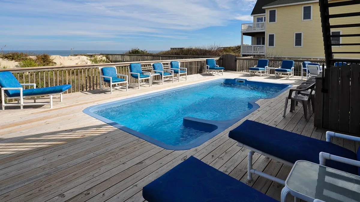 Una piscina al aire libre está en una terraza de madera junto a una casa costera.