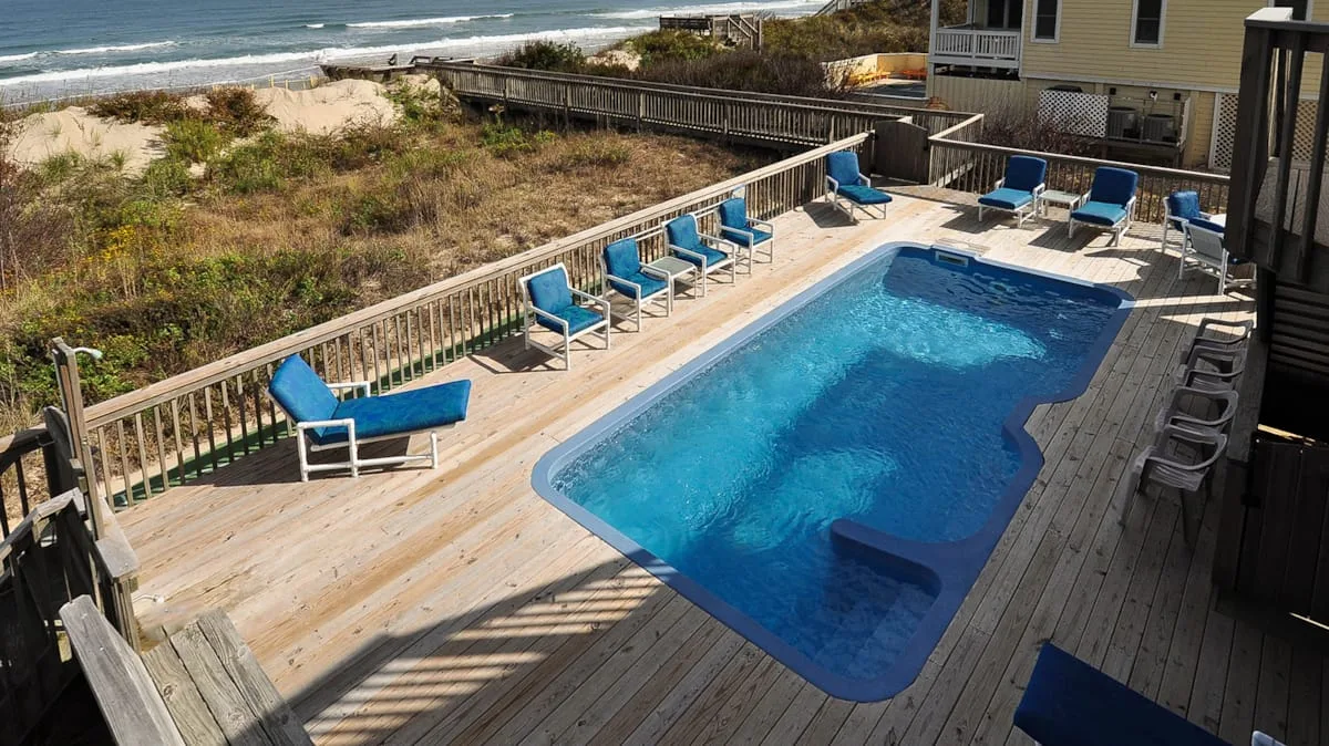 Una piscina al aire libre está sobre una terraza de madera junto a la playa.