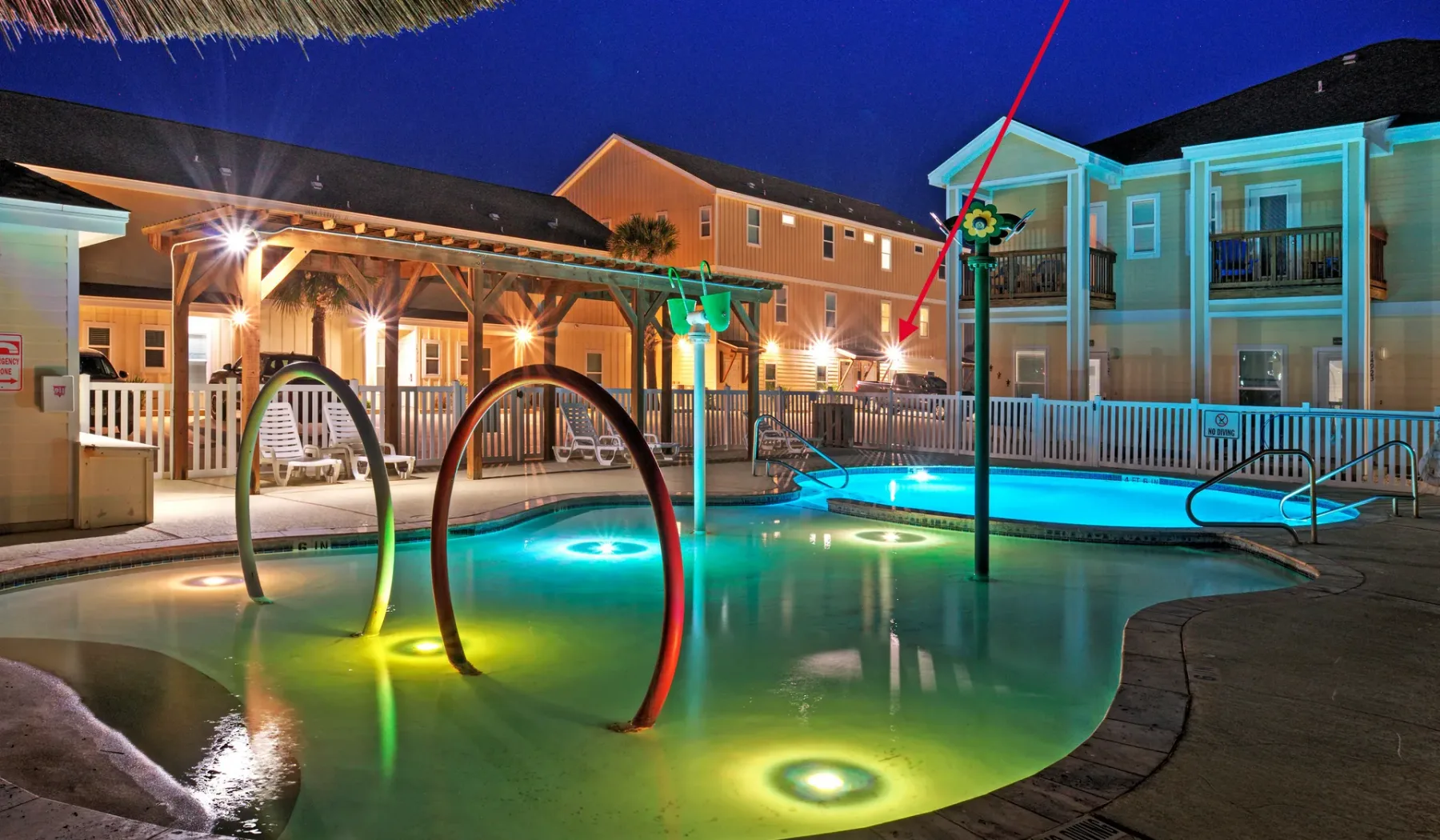 Una piscina iluminada está junto a un patio cubierto por la noche.