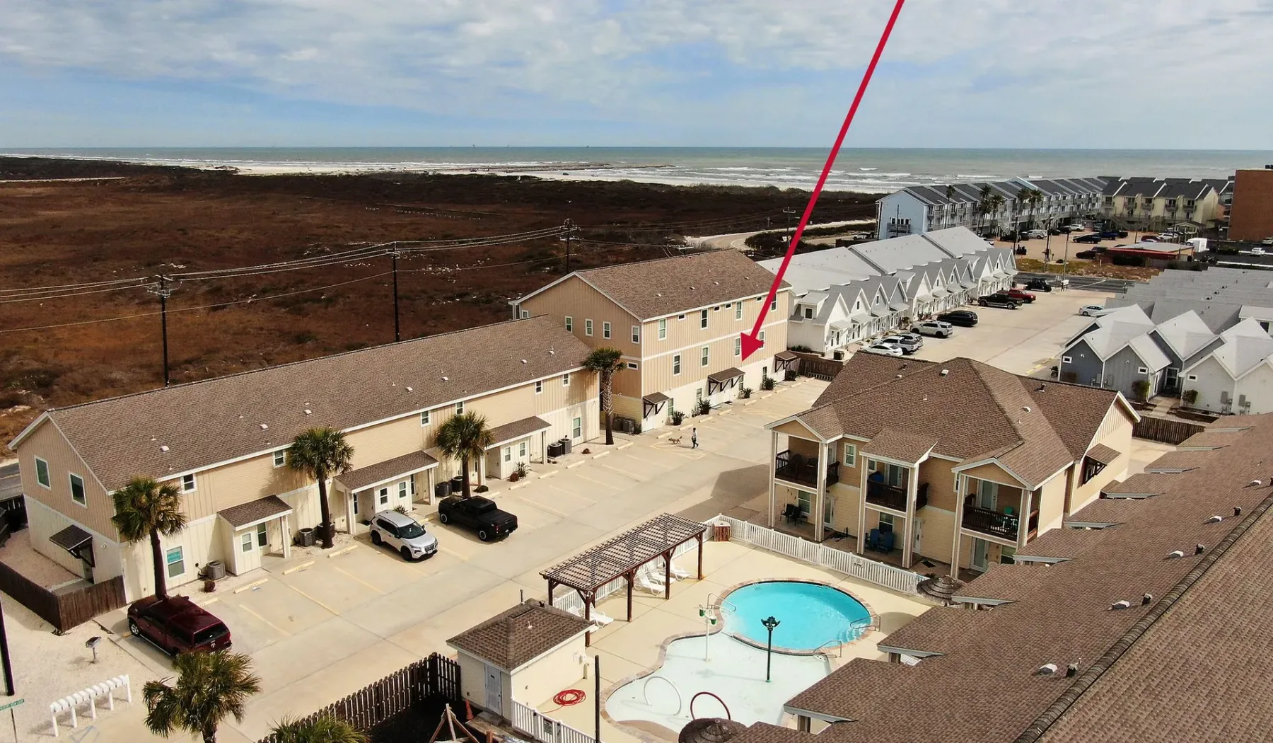 Vista aérea de un complejo residencial costero con piscina y zona de estacionamiento.