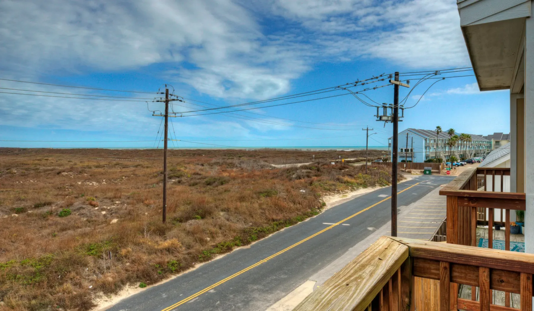 Una terraza de madera da a una carretera costera y terrenos abiertos.
