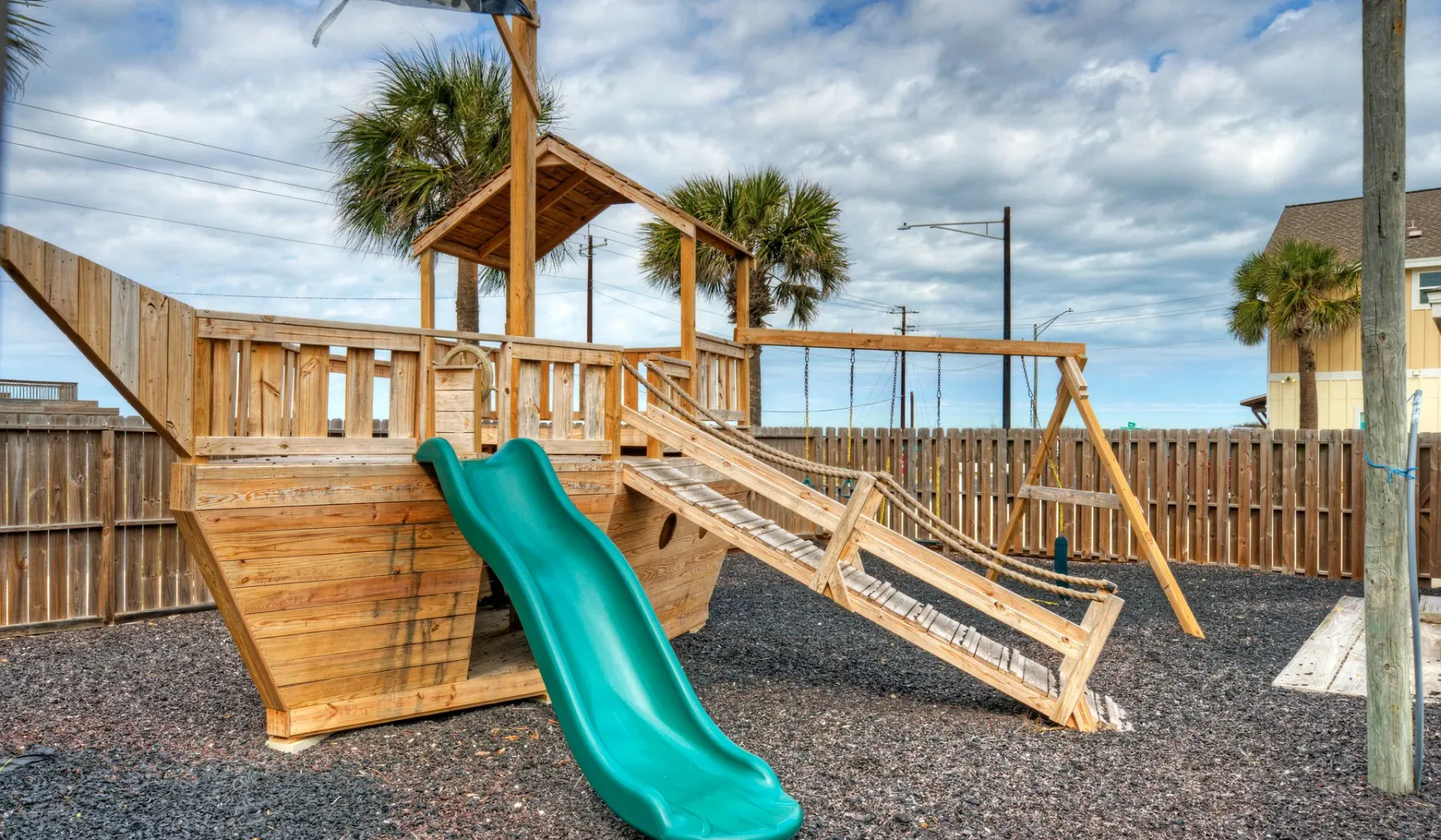 Parque infantil al aire libre con una estructura elevada de madera y un tobogán verde.