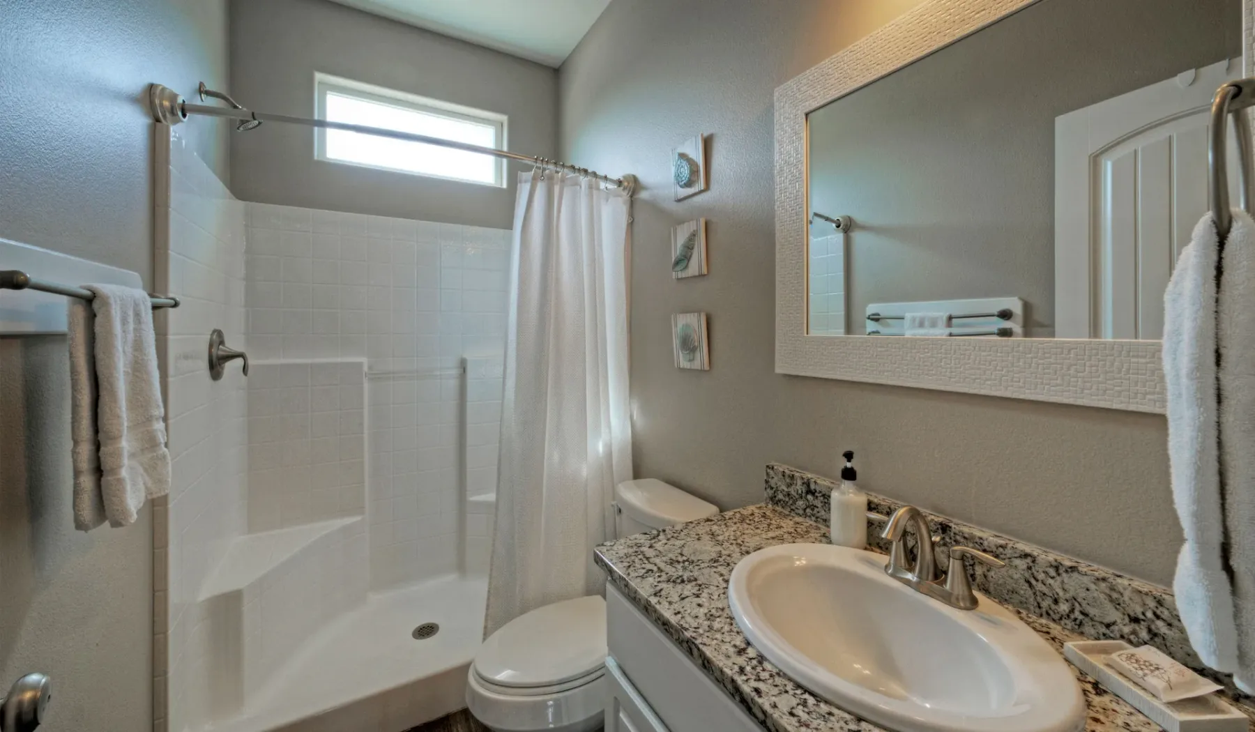 Un baño con ducha, inodoro y lavabo bajo un espejo grande.