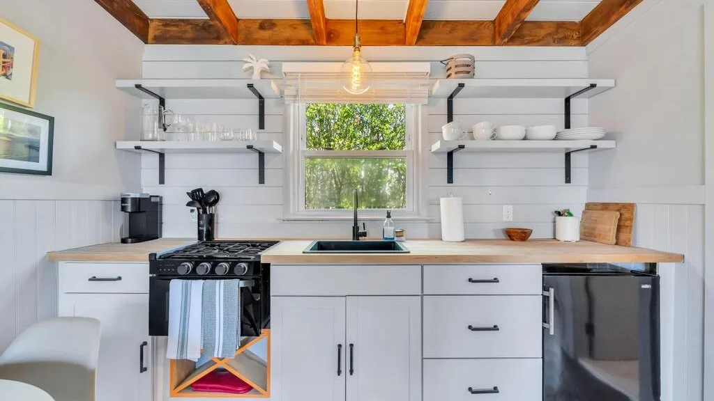 A bright kitchen with white cabinets, open shelves, and a window above the sink.