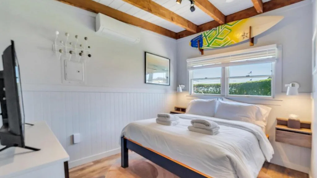 Un dormitorio con una cama bien tendida bajo una ventana amplia.