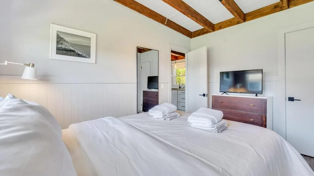 Un dormitorio con ropa de cama blanca, toallas dobladas y un televisor sobre una cómoda.