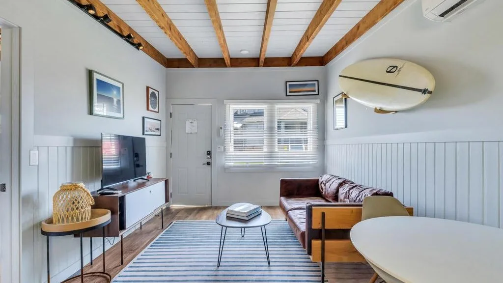 A living room with a striped rug, seating, and a wall-mounted surfboard.