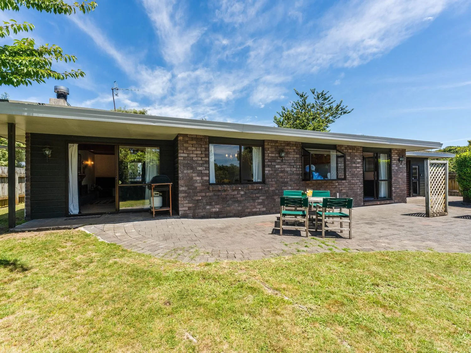 An outdoor patio area with a table and chairs on a paved surface next to a brick house at Lakeside Serenity - Taupo Holiday Home in Rainbow Point