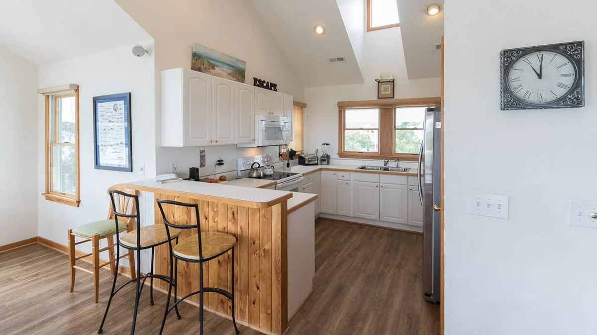Una cocina luminosa con una isla de frente de madera, asientos de barra y ventanas sobre el fregadero.
