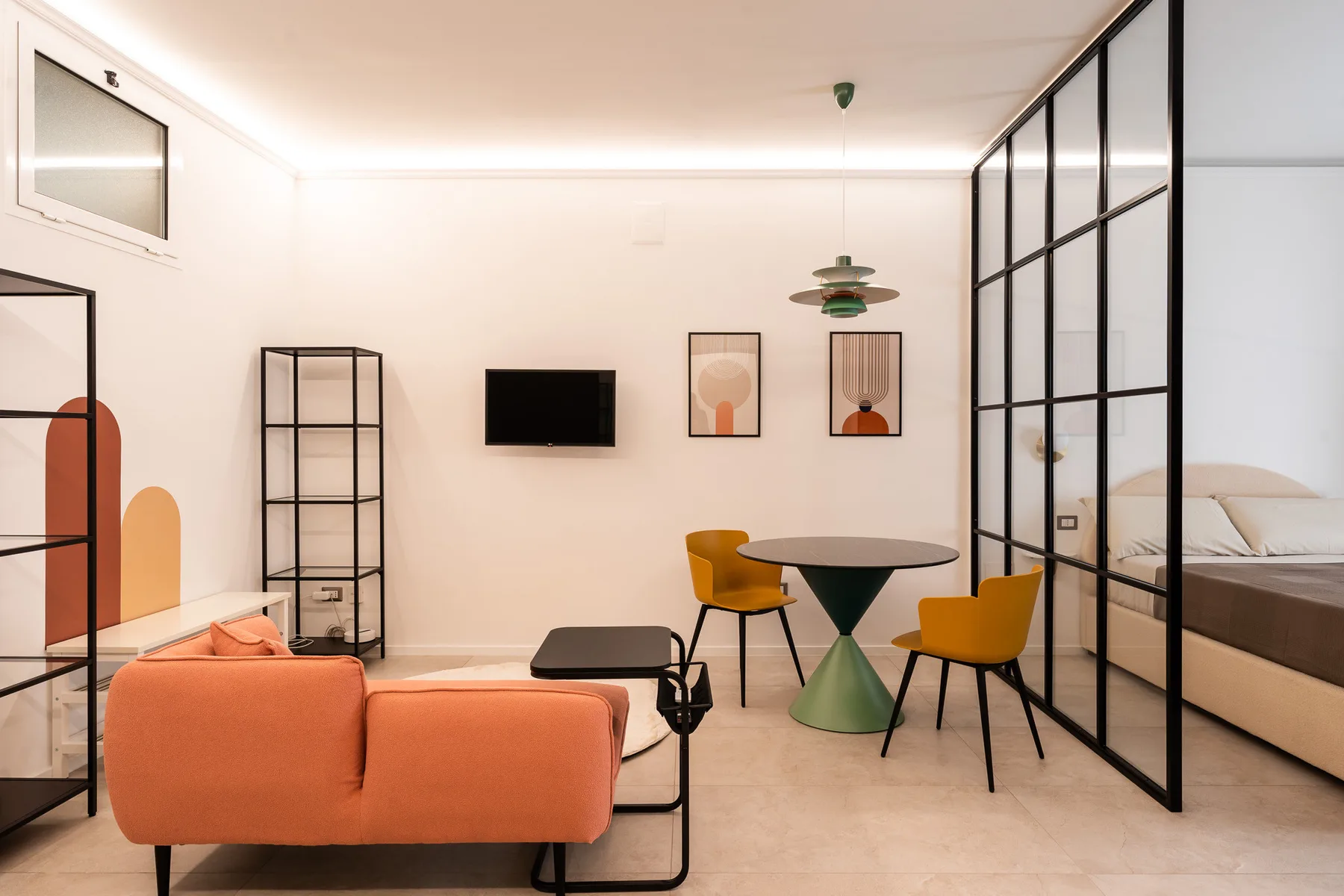 A bright living room with a coral sofa, a small dining table, and glass partitions.