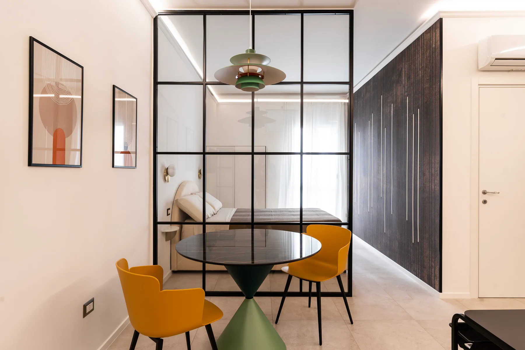 A modern room with a table and chairs, separated from a bed by a glass partition.