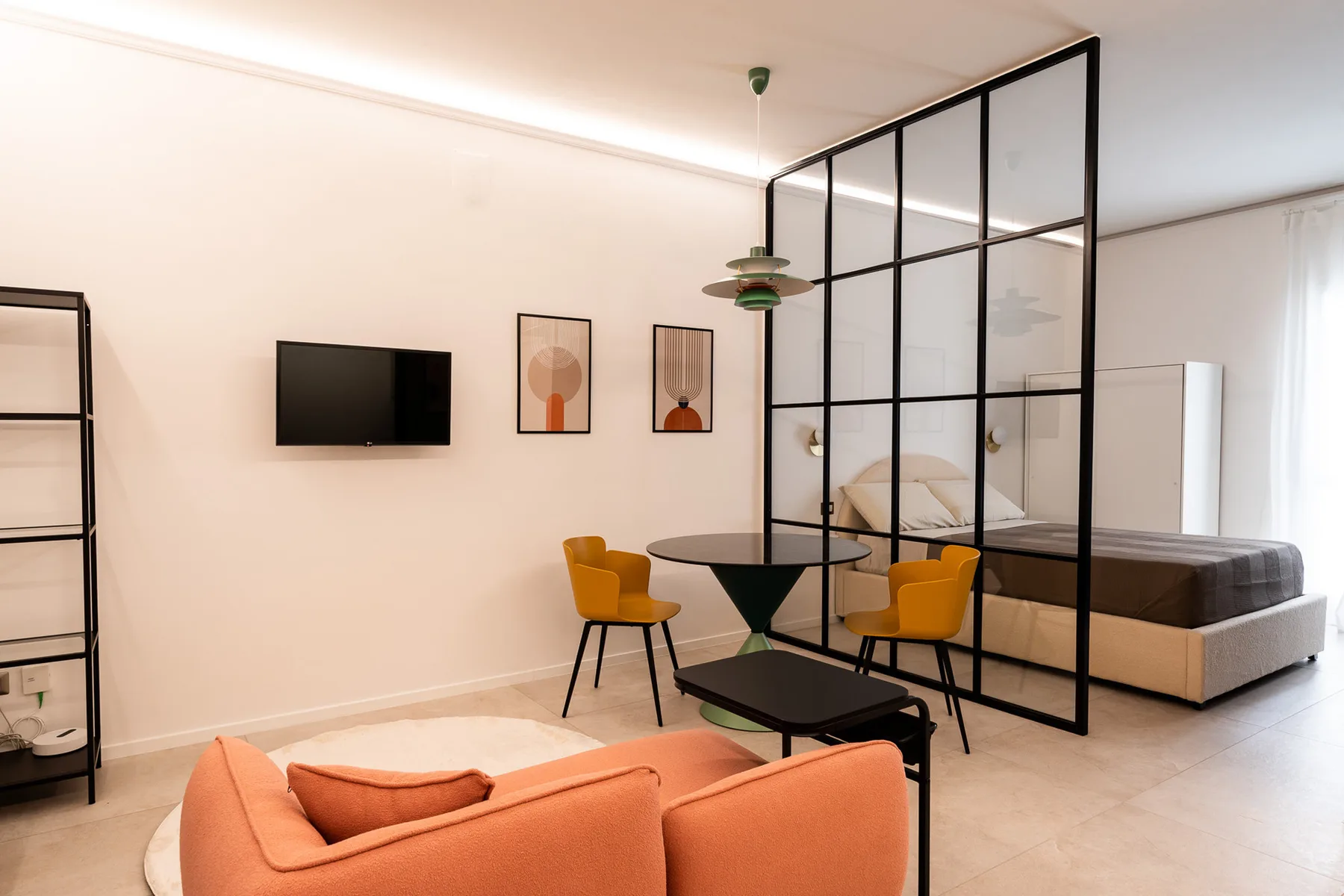 A living and sleeping area with a glass partition and orange seating.