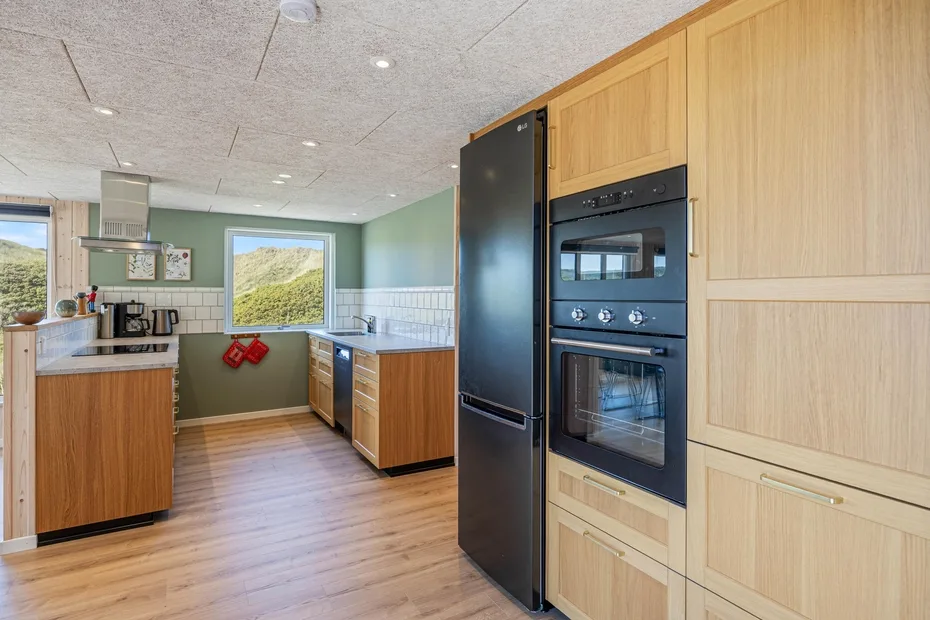 Una cocina luminosa con gabinetes de madera, electrodomésticos oscuros y una ventana con vistas al paisaje verde.