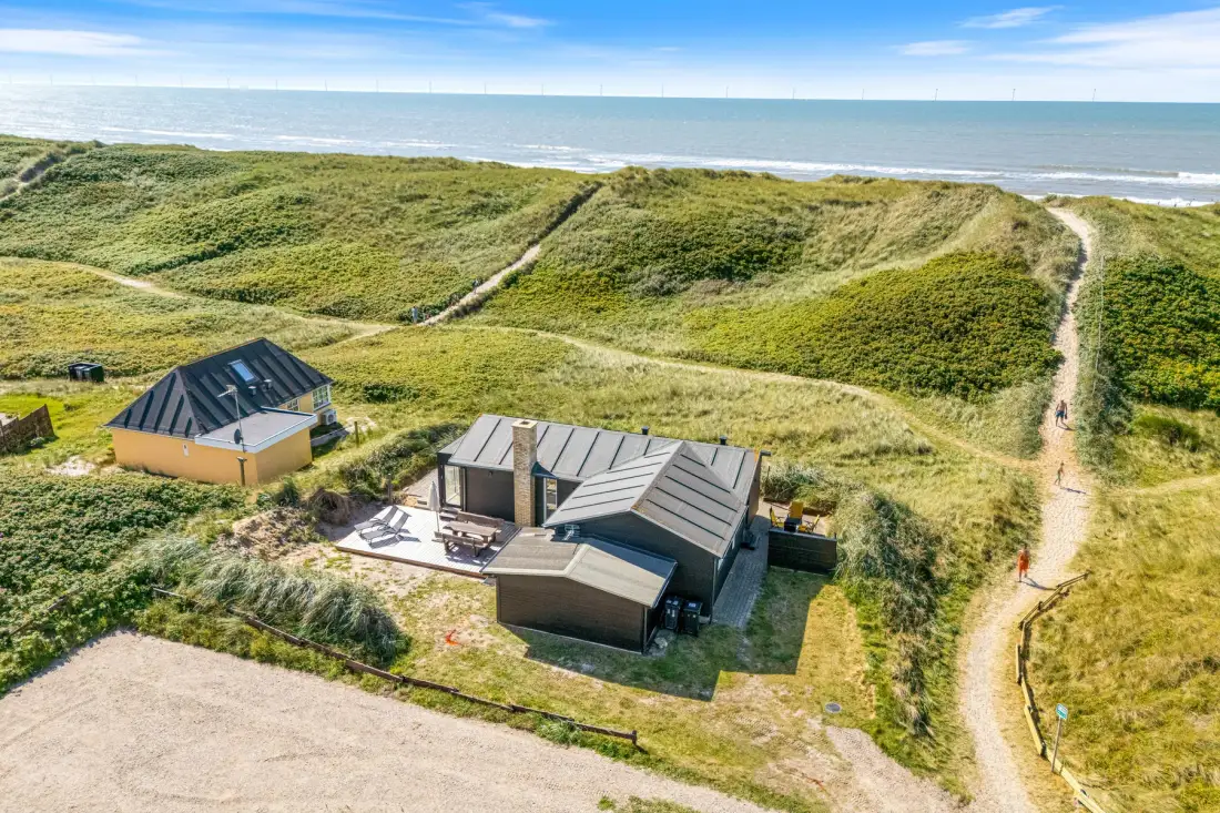 Vista aérea de una casa costera junto a dunas cubiertas de hierba y un sendero.