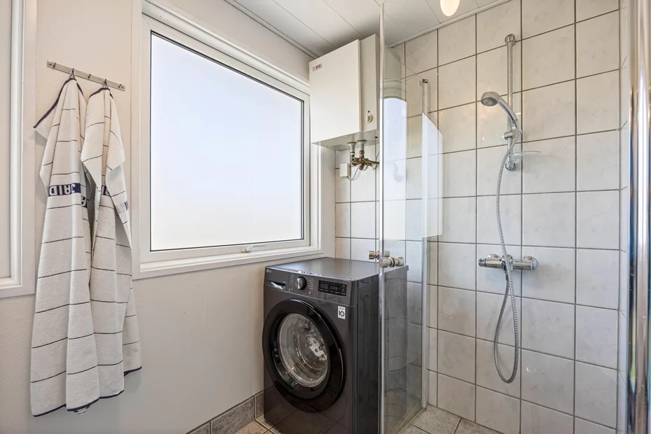 Un baño alicatado con una lavadora junto a la ducha.