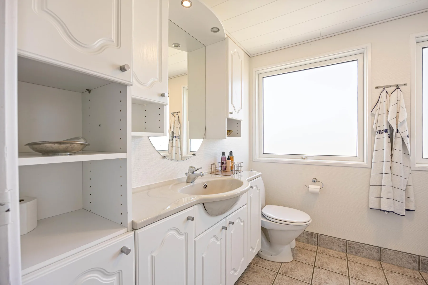 Un baño luminoso con lavabo, inodoro y ventana.