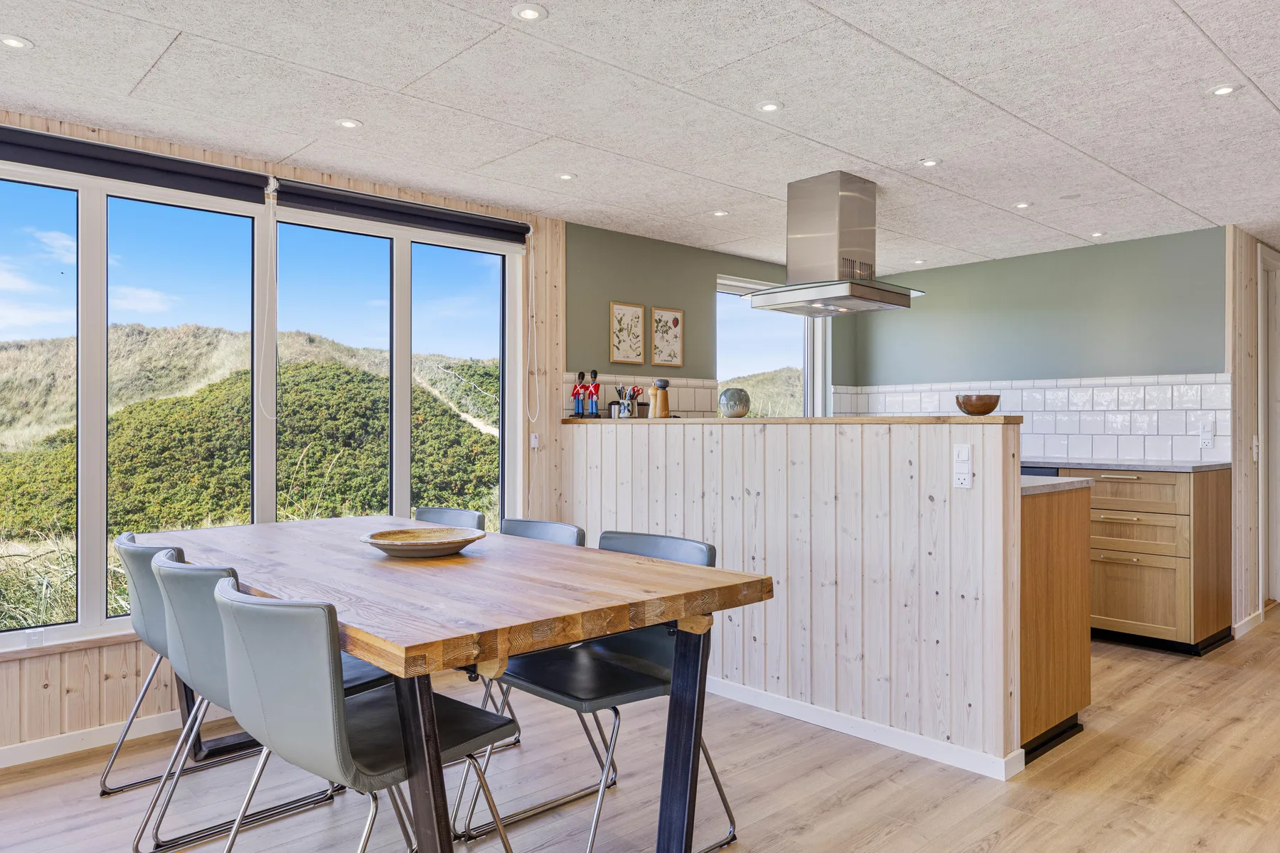 Comedor con una mesa de madera y grandes ventanas con vistas a colinas verdes.