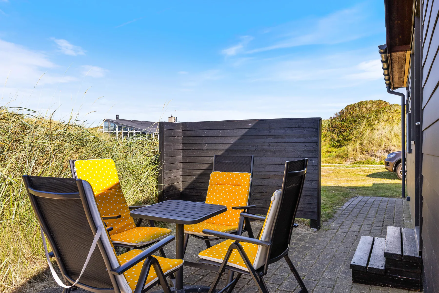 Un patio exterior tiene asientos alrededor de una mesa junto a una pantalla oscura.