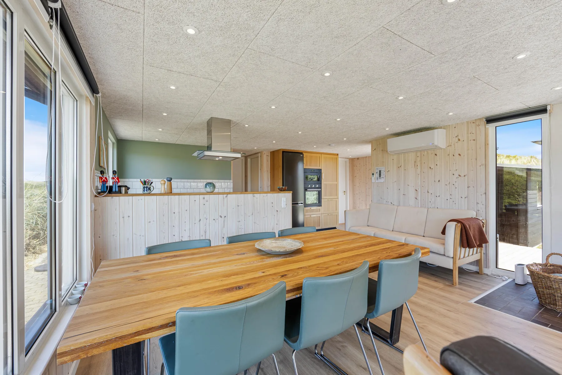 Un comedor y cocina de planta abierta con una mesa larga de madera y asientos azules.