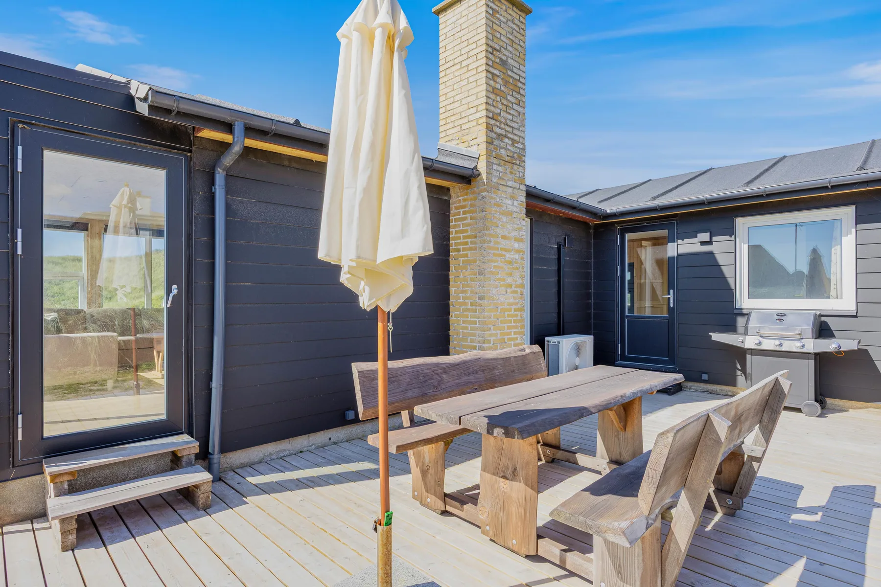 Una terraza de madera con asientos al aire libre y una sombrilla cerrada junto a una casa.