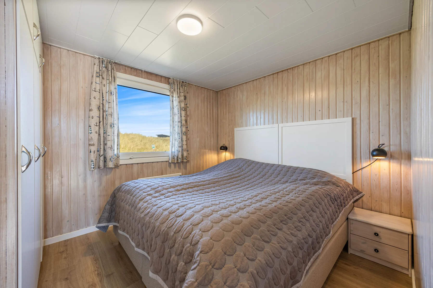 Un dormitorio con una cama bajo un cabecero blanco y una ventana con cortinas.