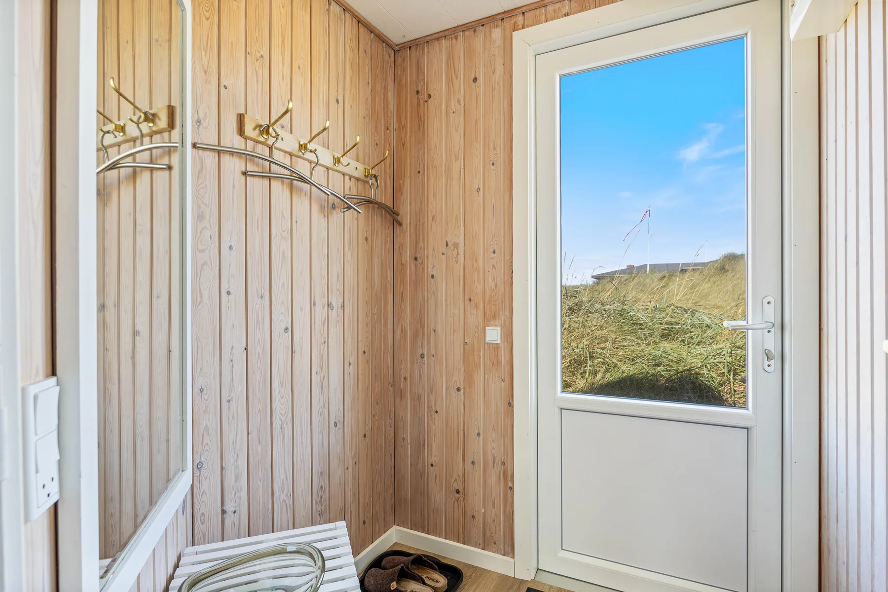 Entrada revestida de madera con percheros de pared y una puerta exterior acristalada.