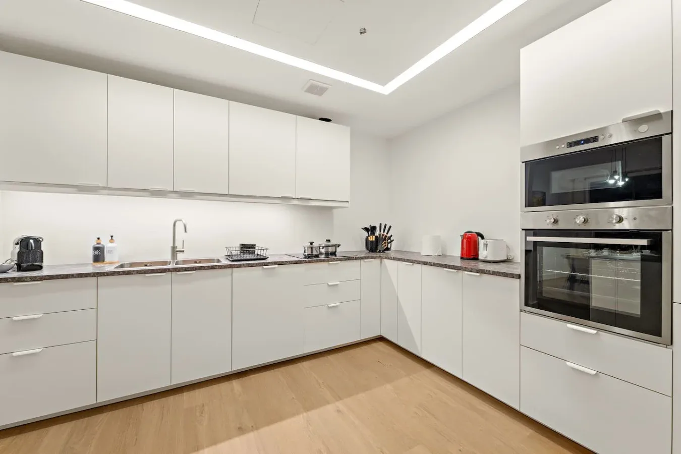 Una cocina moderna y luminosa con gabinetes blancos, encimeras y electrodomésticos integrados.