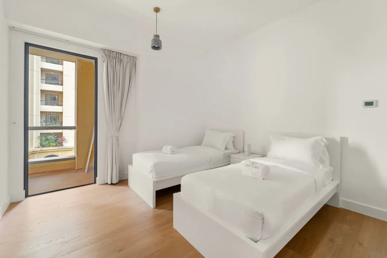 Un dormitorio luminoso con dos camas blancas y una puerta corrediza de vidrio.